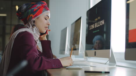 Mujer-De-Negocios-En-Hijab-Hablando-Por-Teléfono-Y-Trabajando-En-La-Computadora